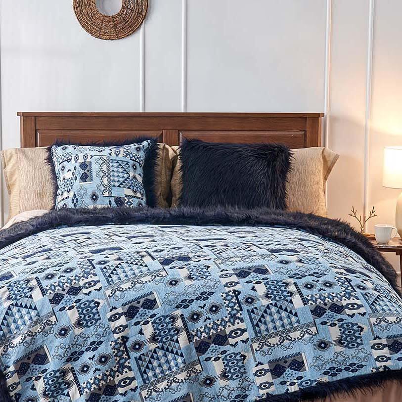 Neatly made bed with a wooden headboard, intricate patterned bedding in blue, black, and white, multiple textured pillows, and a circular woven wall decoration above.