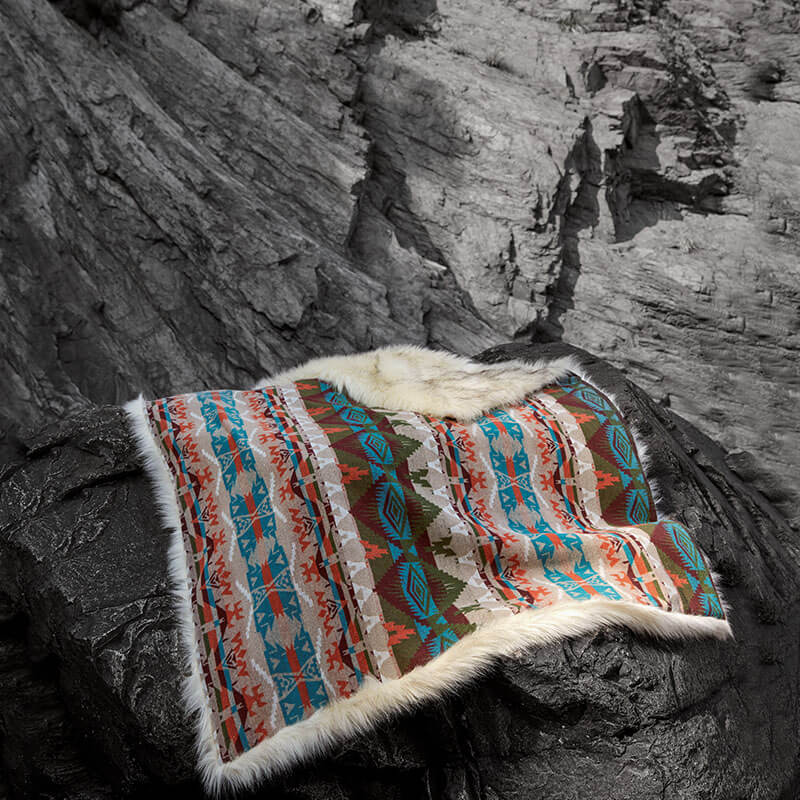 Anifurry turquoise rain dance faux fur blanket laid on the black rocks.