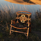Wooden camping chair with Native American-inspired geometric pattern set against a scenic backdrop of rolling hills and a lake.