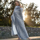 A beautiful woman covered with a gray porcupine faux fur blanket on the ground when the sun sets.
