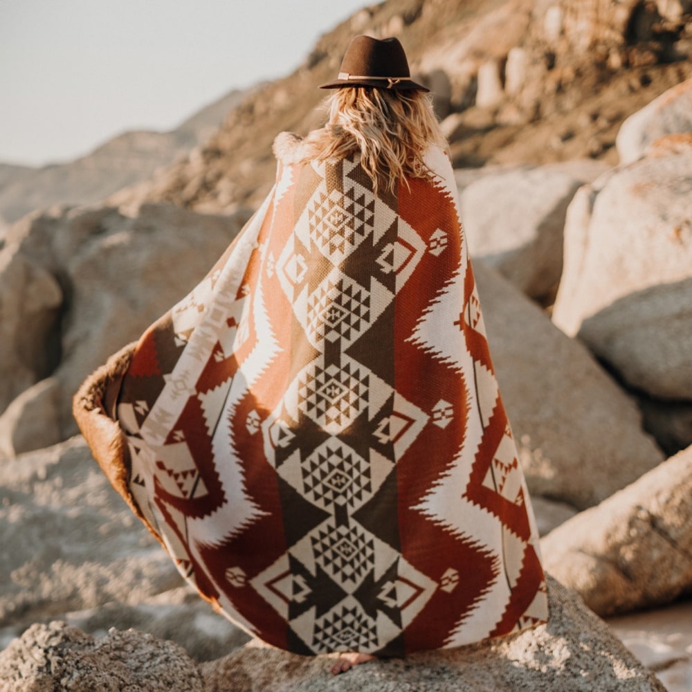 Woman wrapped in a blanket standing on rocky coast.