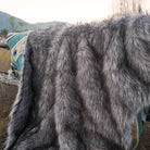 Anifurry gray faux fur blanket is hung on a wooden stake in the wild, and the back of the blanket is an Aztec pattern.