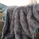 Anifurry gray faux fur blanket is hung on a wooden stake in the wild, and the back of the blanket is an Aztec pattern.