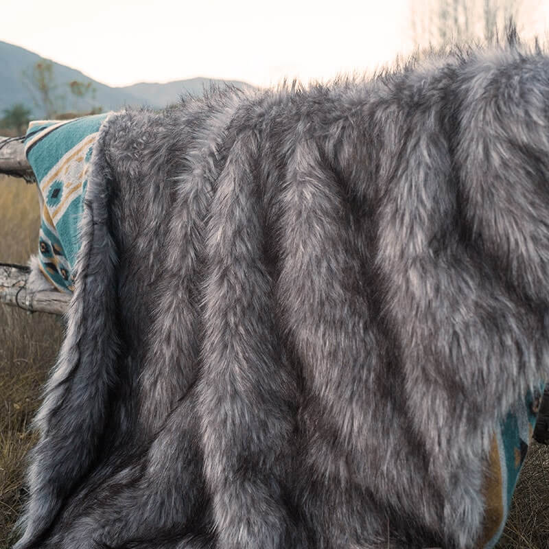 Anifurry gray faux fur blanket is hung on a wooden stake in the wild, and the back of the blanket is an Aztec pattern.