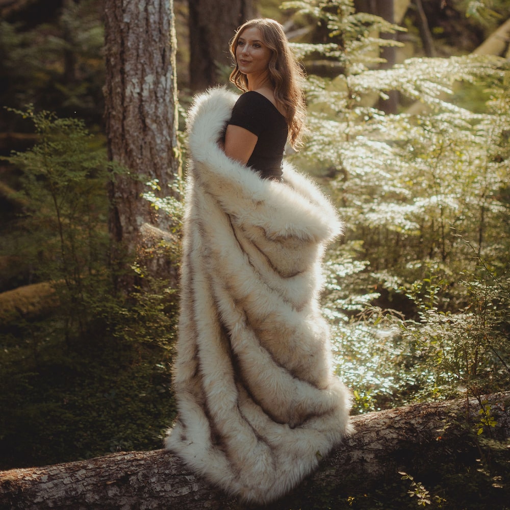A woman, wrapped in a white turquoise rain dance faux fur blanket, stood in the woods.