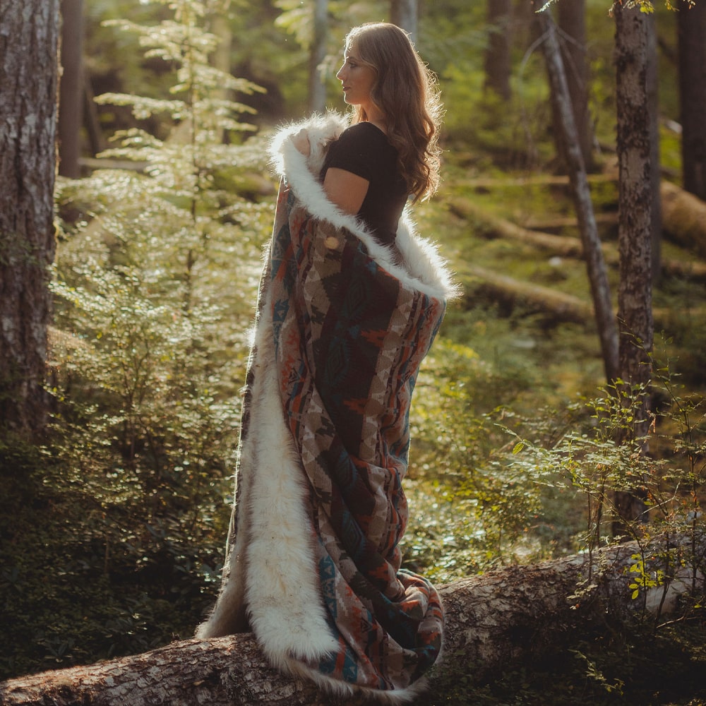 A woman, wrapped in a turquoise rain dance faux fur blanket, stood in the woods.