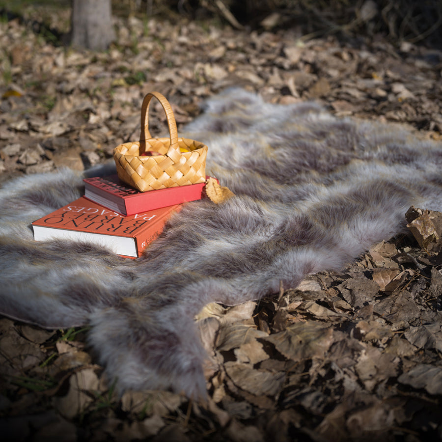The grey faux fur rug is on the ground. It looks extremely fluffy and cozy. A book and a basket are on it. Easy to wash.