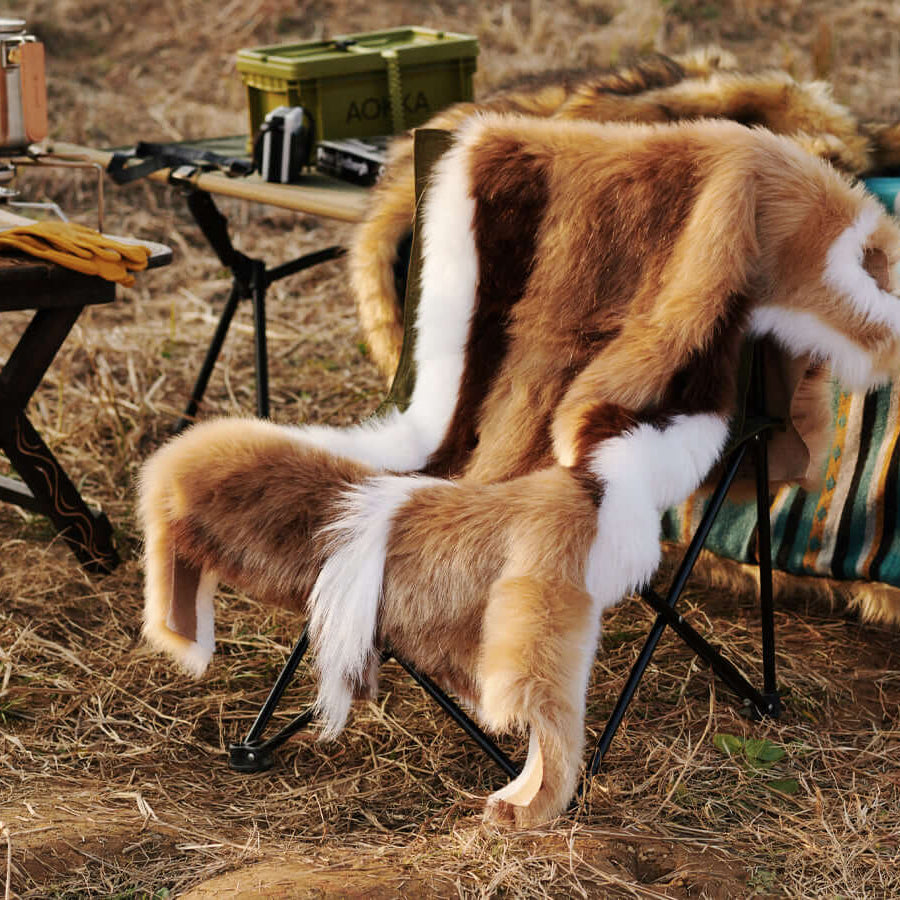 A chair covered by a Faux Impala Pelt Rug, surrounded by Aztec Faux Fur Blanket and wooden tables.