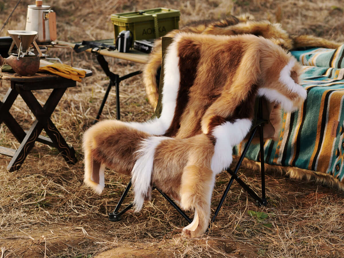A chair covered by a Faux Impala Pelt Rug, surrounded by Aztec Faux Fur Blanket and wooden tables.