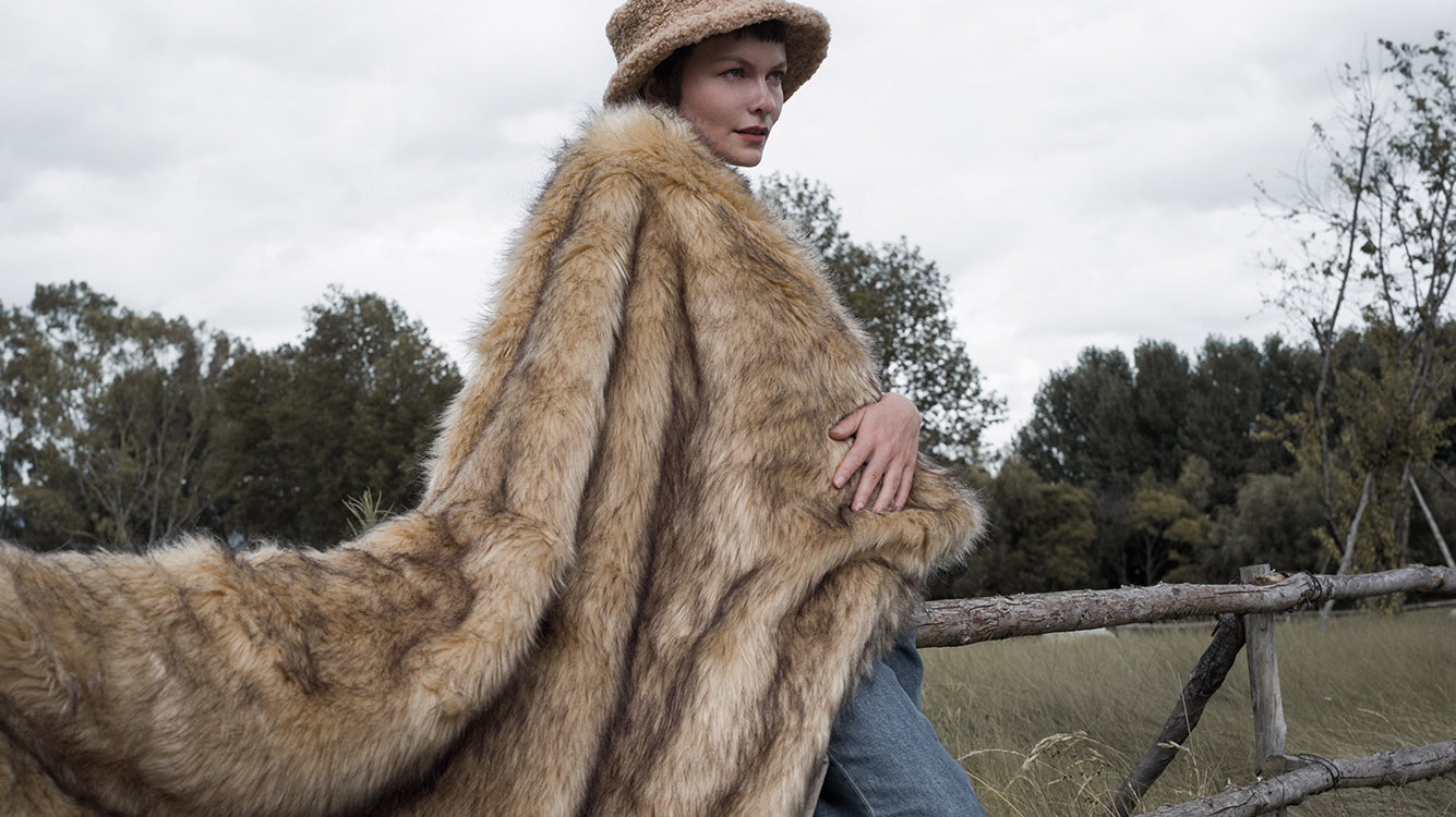 The model wearing a plush and warm golden faux fur blanket. The blanket is multi-functional and easy to wash.