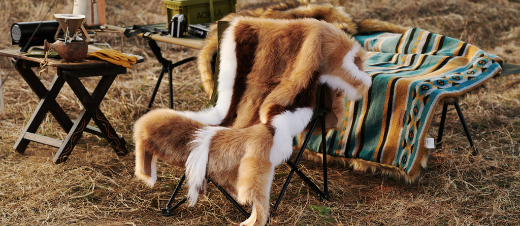 A chair covered by a Faux Impala Pelt Rug, surrounded by Aztec Faux Fur Blanket and wooden tables.