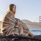 A girl wrapped in a leopard faux fur blanket sits by the river of the Golden Gate Bridge.