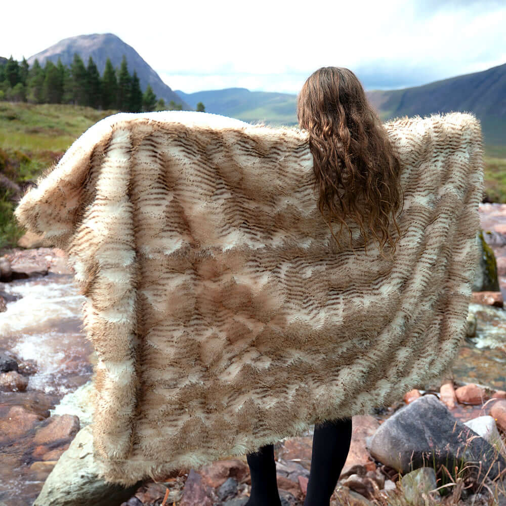A little girl was standing by the stream with her arms outstretched and a jacquard faux fur blanket draped over her.