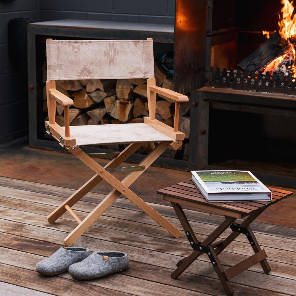 Anifurry Beige Moab Director Chair, small stool, and slippers on a wooden deck in front of a fireplace.