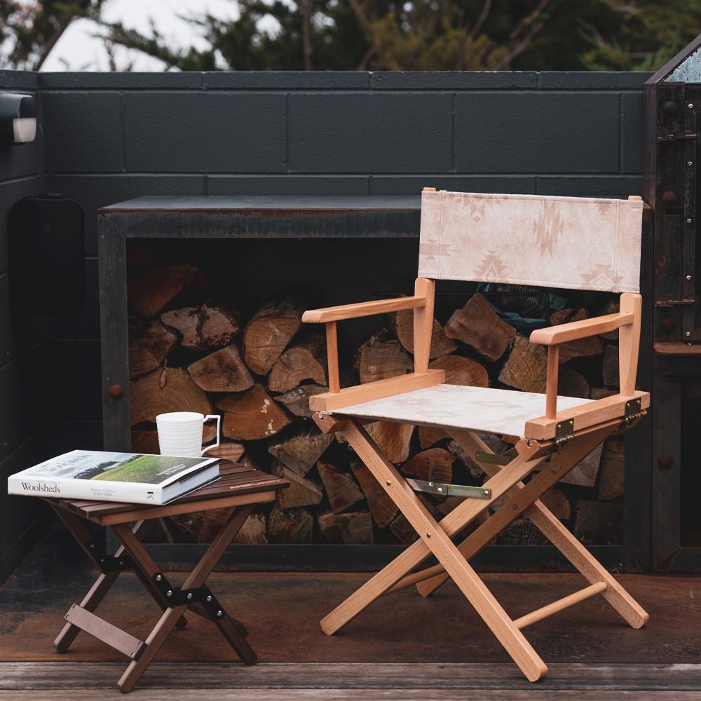 Anifurry Beige Moab Director Chair with a stool against a backdrop of stacked firewood.