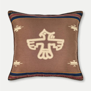A brown wool pillow cover with a beige Thunderbird design and geometric patterns along the borders.