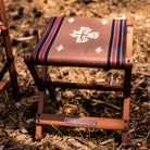Anifurry wood outdoor stool with a patterned thunderbird on a natural ground surface
