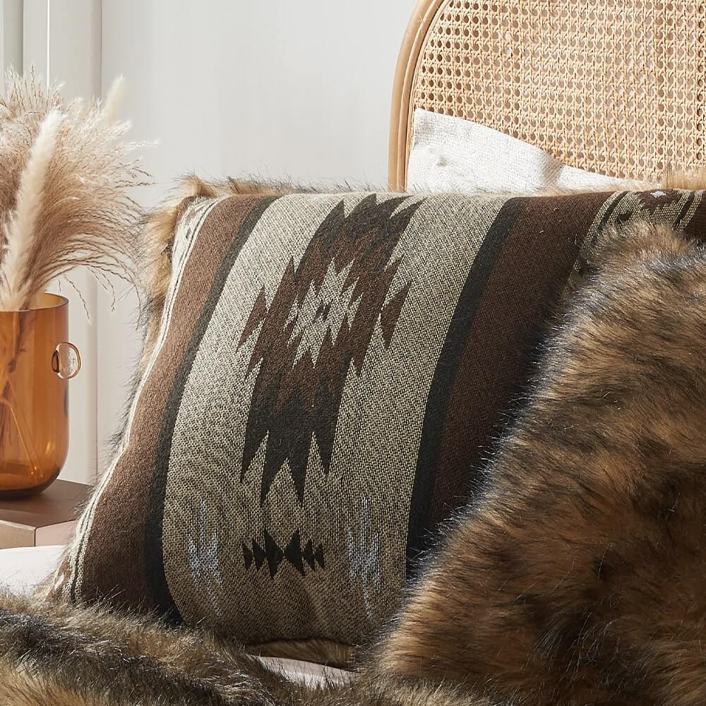The brown aztec pattern on one side and luxurious brown faux fur on the other pillow covers on the bed.
