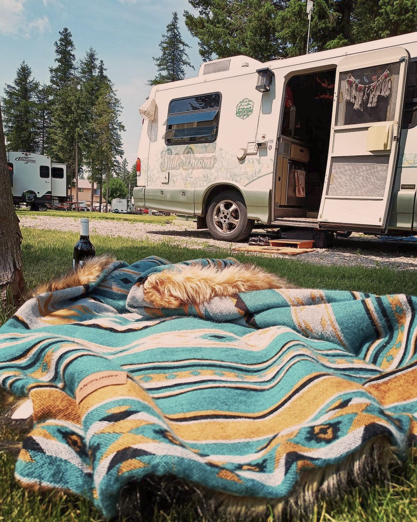There's an RV parked next to a golden ande turquoise aztec fur blanket on the outside lawn