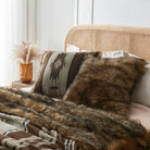 Brown faux fur & brown aztec style pillow cover on a bed with a same color faux fur blanket.