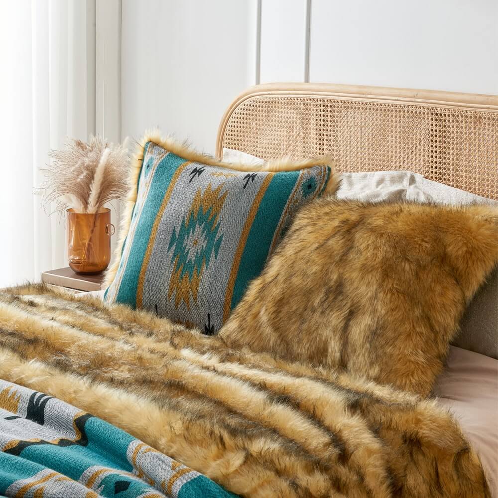 Golden faux fur & Turquoise aztec style pillow cover on a bed with a golden faux fur blanket.