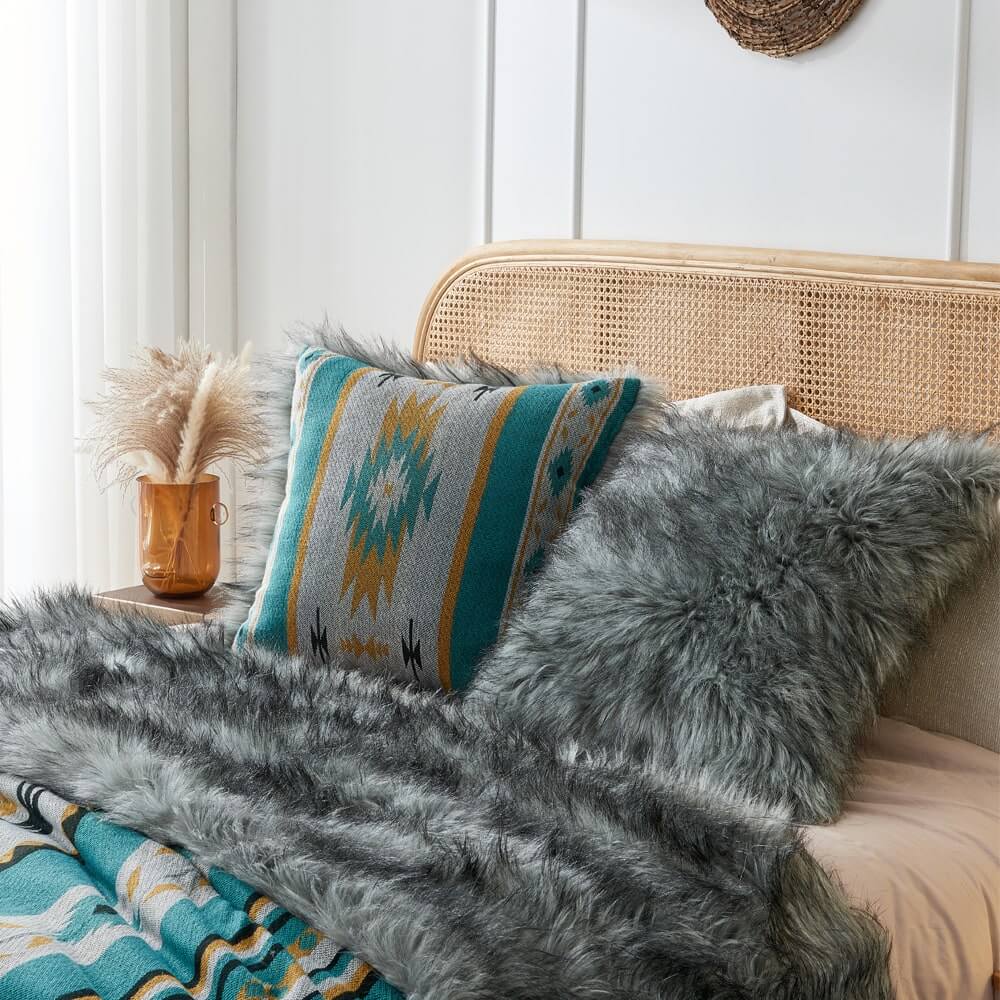 Grey faux fur & Turquoise aztec style pillow cover on a bed with a grey faux fur blanket.