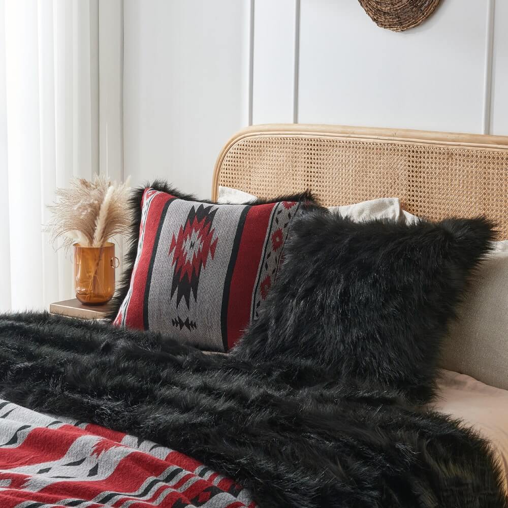 Black faux fur & Red aztec style pillow cover on a bed with a same color faux fur blanket.