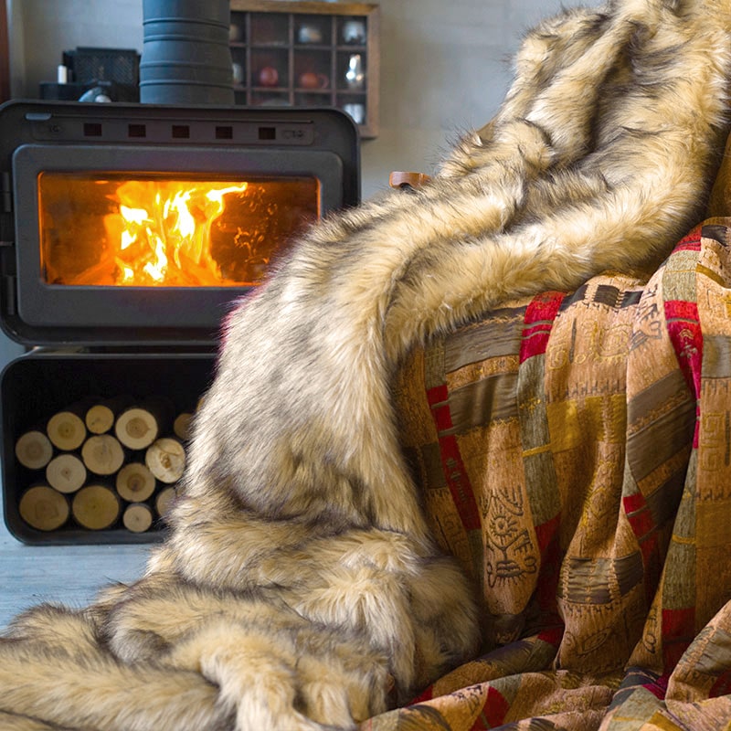 The soft golden faux fur blanket is on the chair beside the fireplace. It has one fur side and one totem pattern side.
