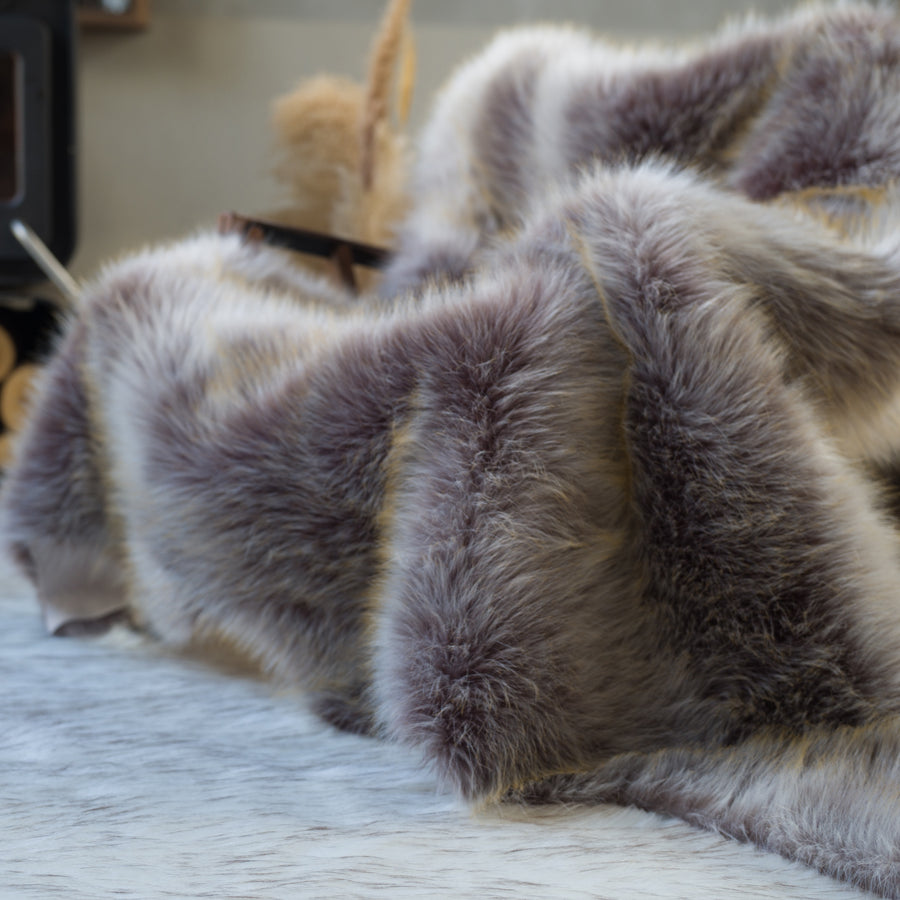 The grey faux fur rug is on a chair. The high-quality rug is reversible and suitable for home decor. Easy to wash and store.