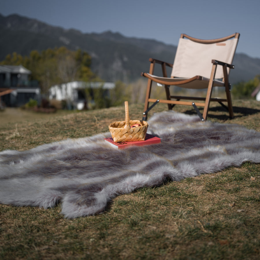 The rich-textured grey faux fur rug is on the ground. One chair is on it. Great decoration for both home anc camping.