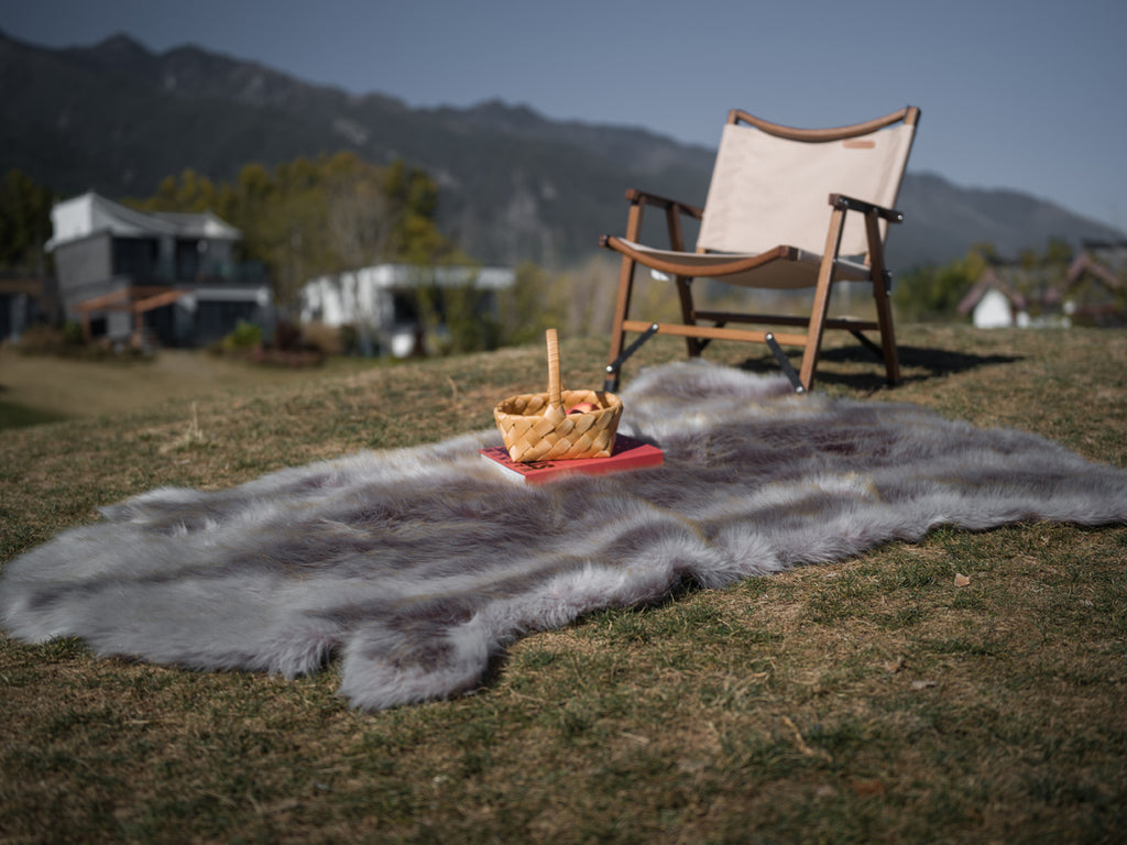 The rich-textured grey faux fur rug is on the ground. One chair is on it. Great decoration for both home anc camping.