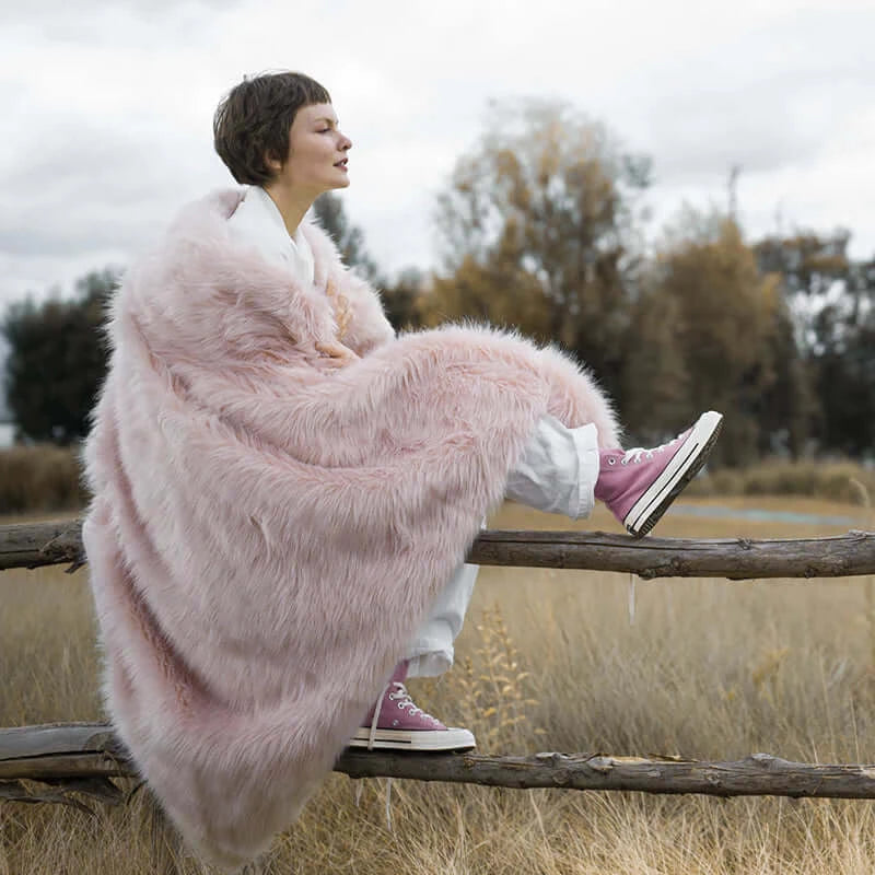 The model wearing an extremely soft pink faux fur blanket. The blanket is machine washable and easy to clean.